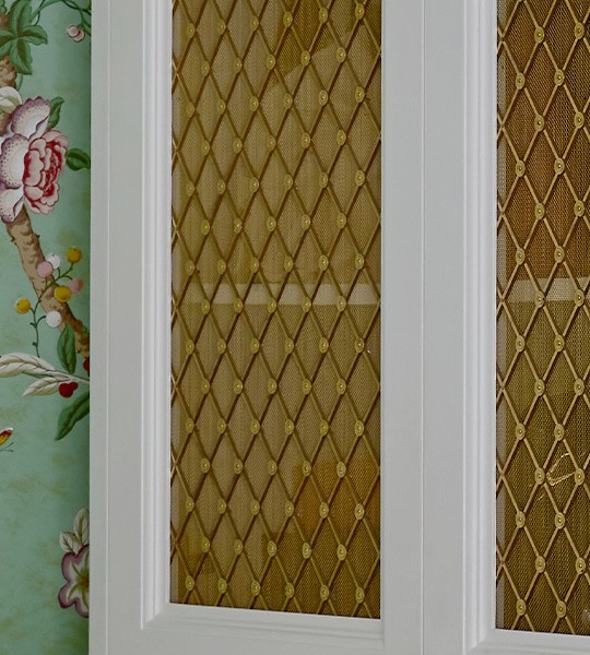 White cabinet front frames inset with best woven metal decorative grilles in basketweave pattern with mesh backing.