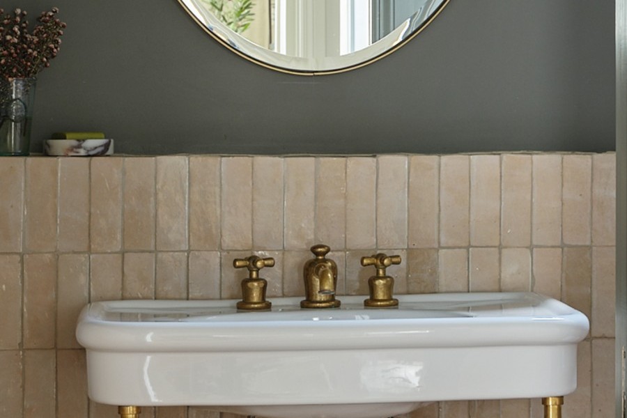 Close up of traditional brass bathroom taps with crosshead handles and spout with pop up waste exhibits natural aging patina.