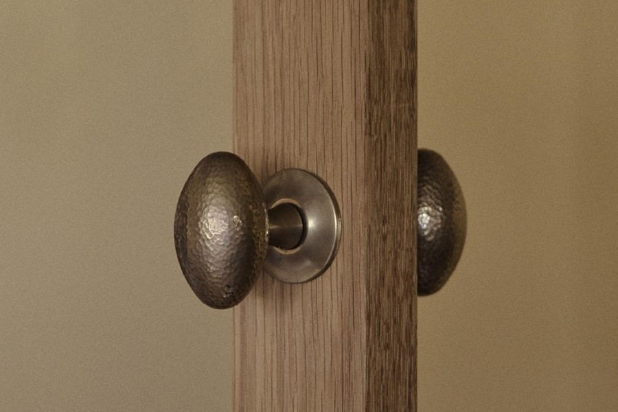 Joseph Giles intricate hammered brass oval doorknobs from the English Tapware Company on a timber door. 