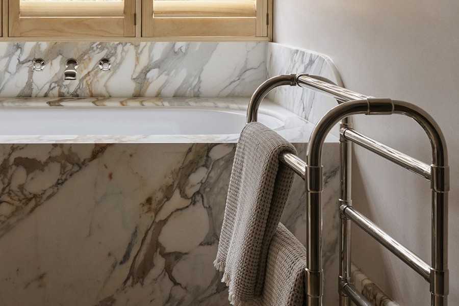 A traditional towel rack next to a marble bath featuring Perrin & Rowe traditional hot and cold taps from The English Tapware Company.