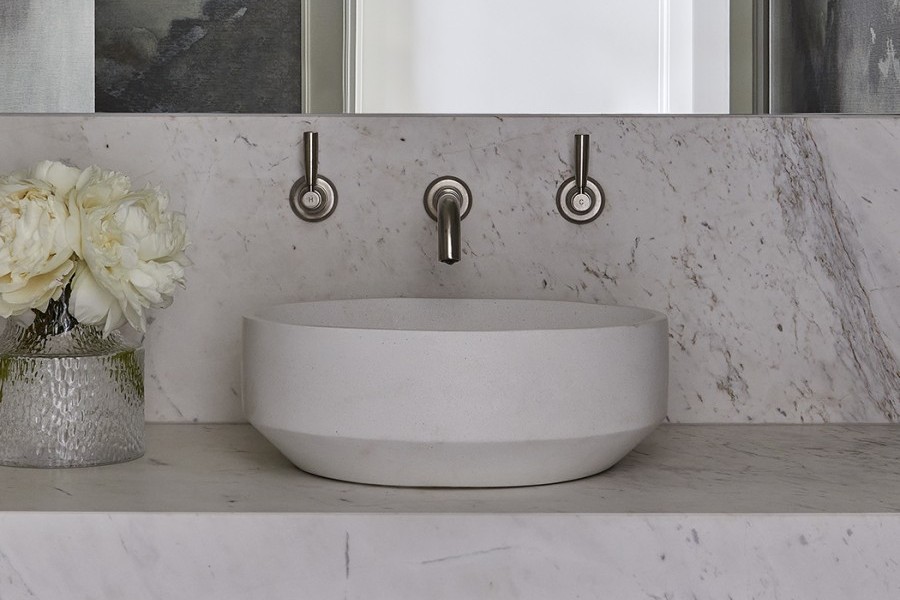 Pewter bathroom taps are wall mounted above stone vessel bowl basin on top of marble vanity in contemporary powder room.
