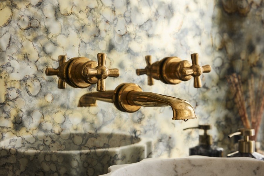 Powder room featuring polished brass tapware, grey Rockwell toilet pan, black marble vanity, and champagne floral wallpaper creating a bold yet elegant design