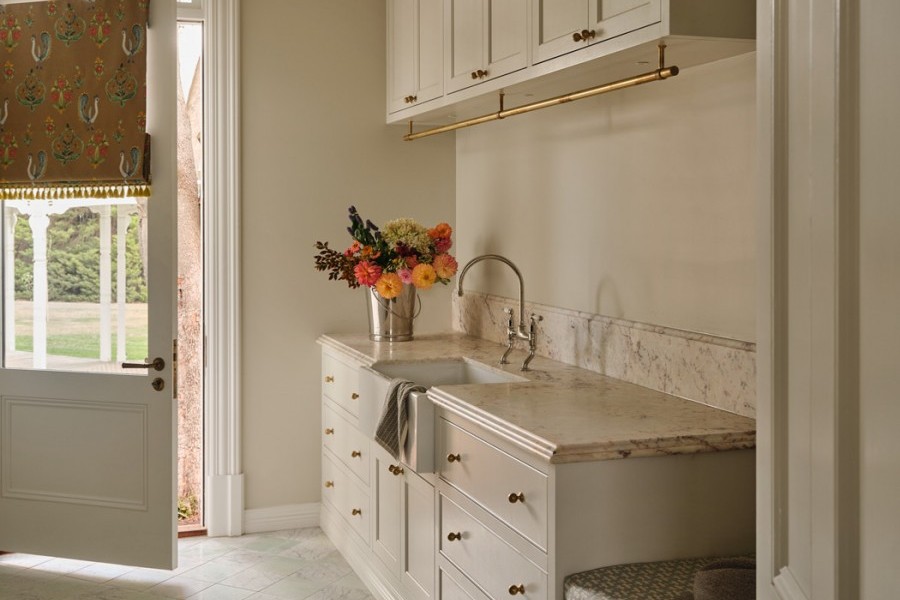Laundry with soft cream and warm beige tones, Joseph Giles brass hanging rails, Perrin & Rowe tapware, and Armac Martin cabinetry opening toward the garden.