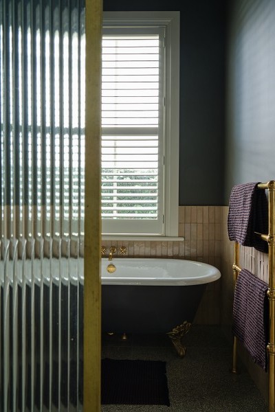 Raw brass towel warmer and brass bath taps complement black and white roll top bath with traditional claw feet.
