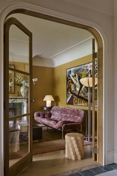 Timber arched doors lead into a yellow living room, with Joseph Giles intricate hammered brass oval doorknobs.