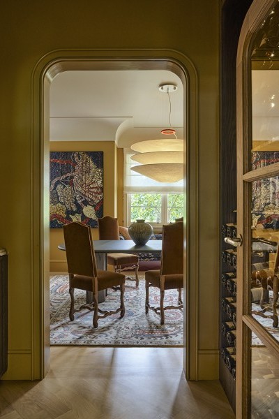 A door with a Joseph Giles hammered brass oval doorknob opens into a wine cupboard and a yellow dining room beyond. 