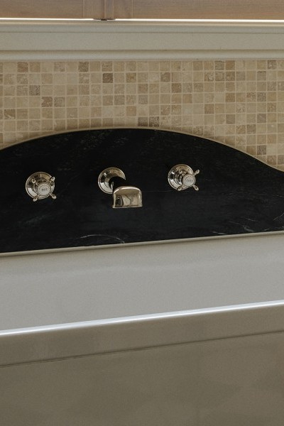 A white bath and green marble backsplash with Perrin & Rowe polished nickel wall-mounted traditional tapware.