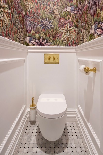 Polished brass toilet flush plate, brass and ceramic wall mounted toilet brush and brass toilet roll holder in toilet.
