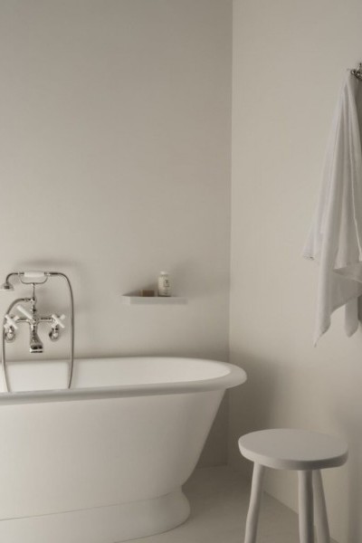 Freestanding bathtub with nickel and white tapware, wall mounted stone soap dish, robe hook with white towel and small white stool. 