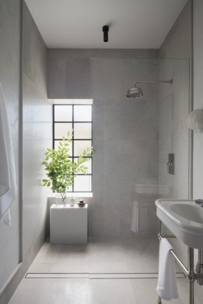 White wall mounted porcelain basin and nickel basin stand, with nickel and blue cross handle tapware. Wall mounted overhead showered in background and white towel on robe hook. 