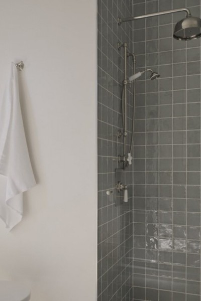 Shower area with wall mounted overhead shower head, single lever shower mixer and sliding rail. Robe hook placed outside shower with white towel, all in nickel finish.