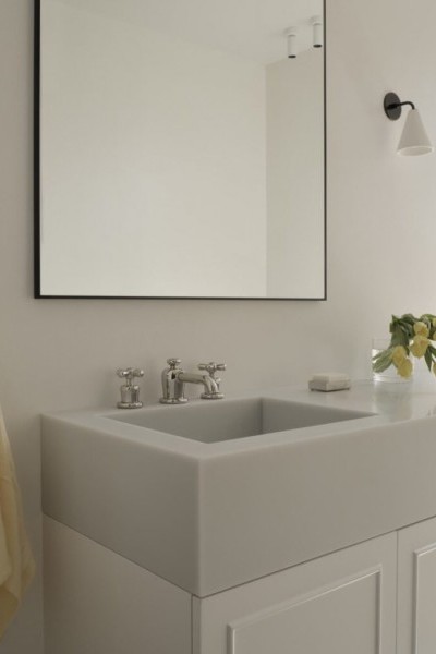 Custom vanity with grey stone sink, white cabinetry and nickel tapware under thin black framed mirror. 