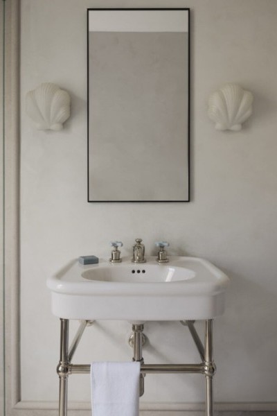 White wall mounted porcelain basin and nickel basin stand, with nickel and blue cross handle tapware. Blue soap, shell wall lights and thin black framed mirror. 