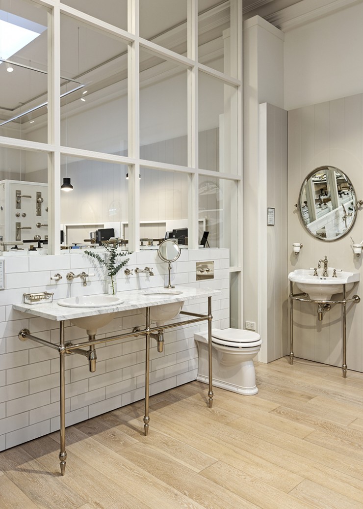 Twin basins recessed into marble vanity top supported on traditional metal basin stand in bathroom retail showroom.