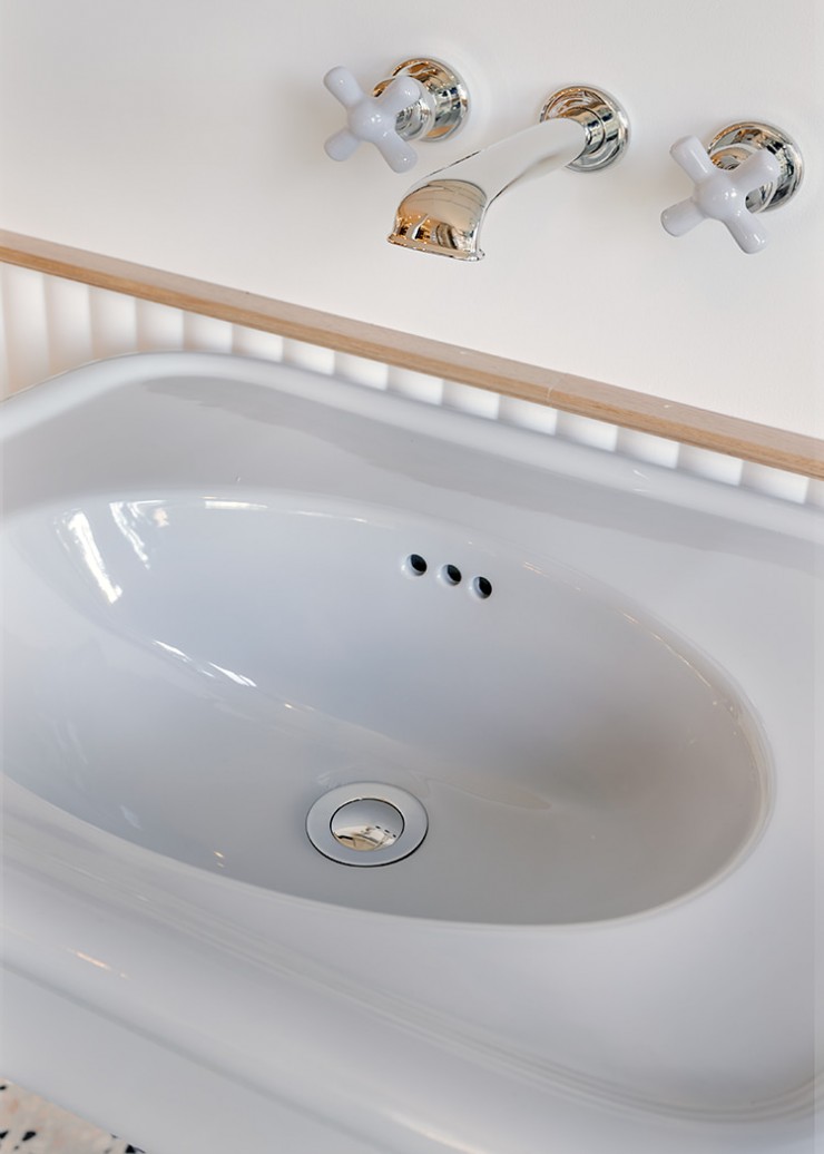Close up of  grey crosshead basin taps wall-mounted with traditional style basin spout in nickel above grey basin.