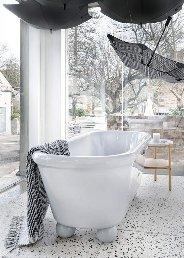 Shop window display featuring Blunt umbrellas suspended over grey  freestanding bath on round bath feet.
