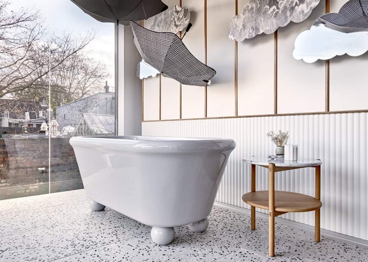 Freestanding grey bath on round ceramic bath feet situated on grey and black terrazzo floor in bathroom showroom display.