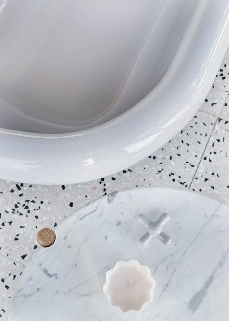 Close up of grey ceramic crosshead tap handle sitting on marble coffee table beside curved rim of grey bath tub.